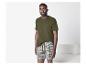 Man in een olijfgroen T-shirt en gestreepte boxershort, staand in een kamer.