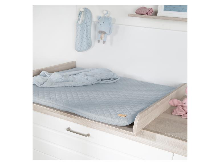 Commode met een blauw gewatteerd kussen, deken en knuffels.