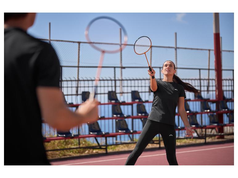 Vrouw en man spelen badminton op een buitenbaan, gekleed in zwarte sportkleding.