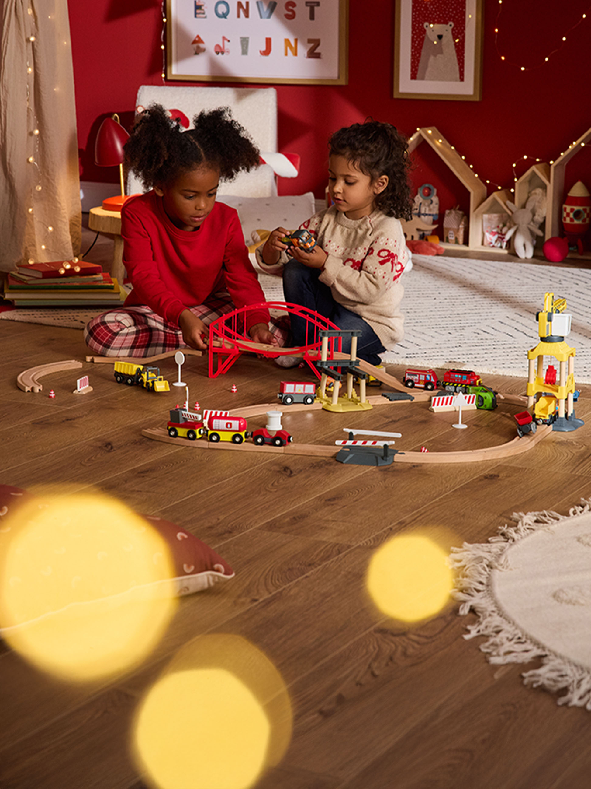 Twee kinderen spelen met een houten treinset en voertuigen op een houten vloer.