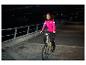 Vrouw in roze fietsjack rijdt 's nachts op een elektrische fiets.