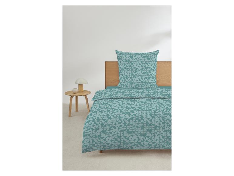 Beddengoed met geometrisch patroon in turquoise tinten, op een houten bed met nachtkastje.