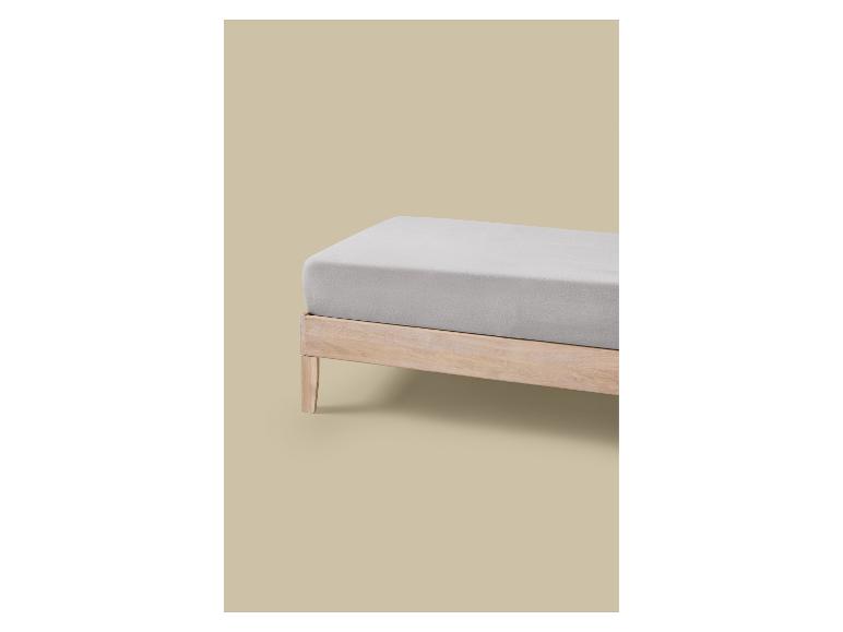 Een bed met een licht houten frame en grijs matras