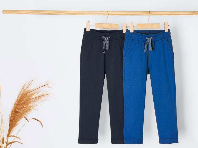 Twee blauwe en zwarte joggingbroeken hangen aan een houten hanger.