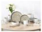 Elegant eetservies met gespikkelde borden, kommen, mokken en bestek op een lichte houten tafel.