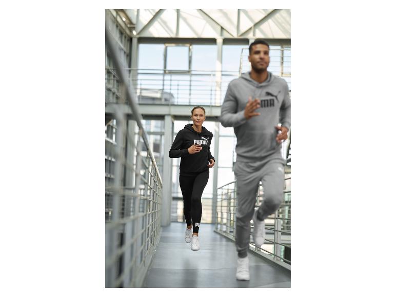 Twee mensen joggen binnen, gekleed in zwarte en grijze sportieve hoodies en joggingbroeken.