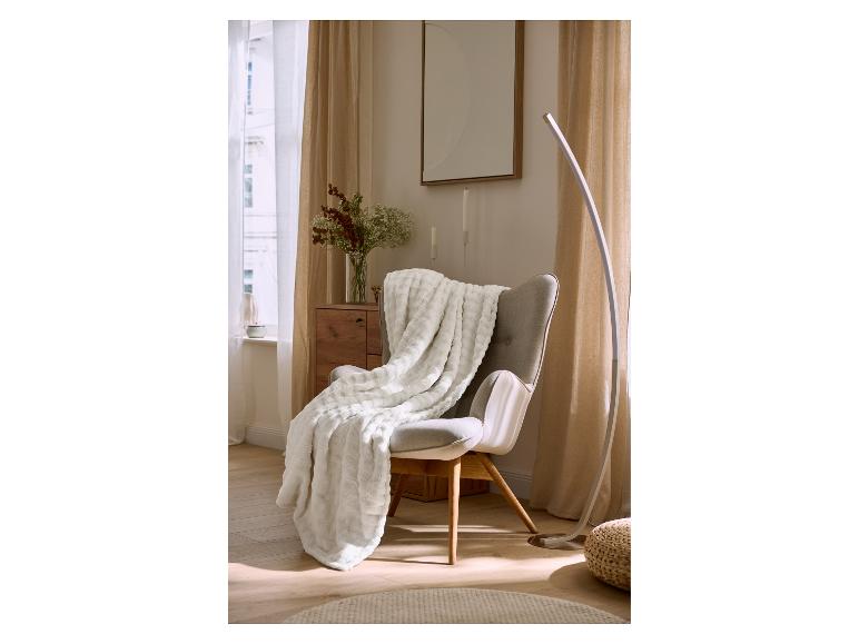 Grijze fauteuil met witte deken en moderne vloerlamp in een gezellige kamer.