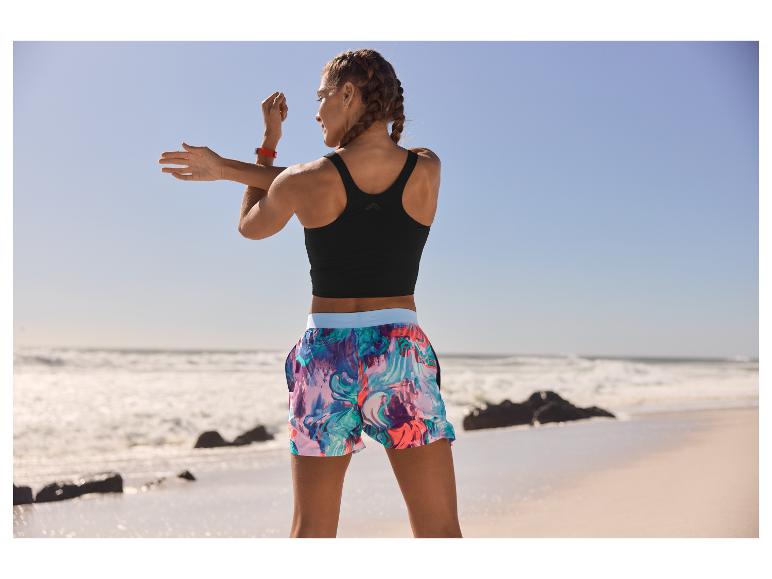Vrouw in sportbeha en short aan het strand.