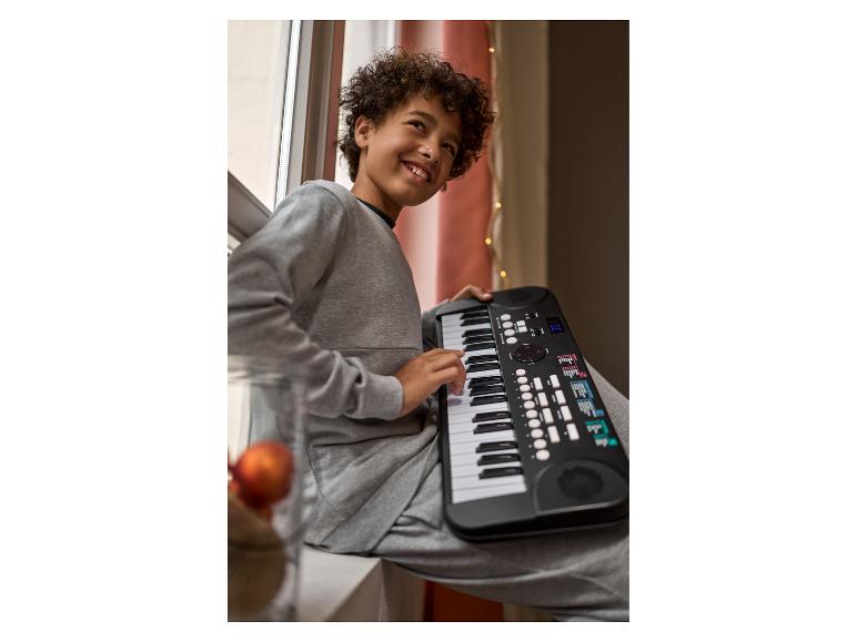 Jongen zit bij het raam en speelt op een zwarte elektronische piano.