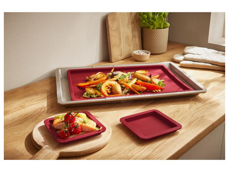 Rode siliconen bakvormen en bakplaten op een houten oppervlak.