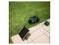 Groene robotmaaier met laadstation en zonnepaneel in een tuin.