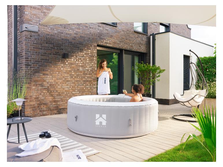 Twee vrouwen genieten van een grijze opblaasbare hot tub op een terras bij een bakstenen huis.