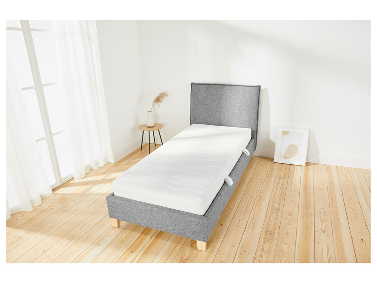 Een grijs bedframe met een wit matras op een houten vloer.
