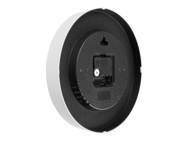 Achterkant van een zwart-witte wandklok met kwartsuurwerk en batterijvak.