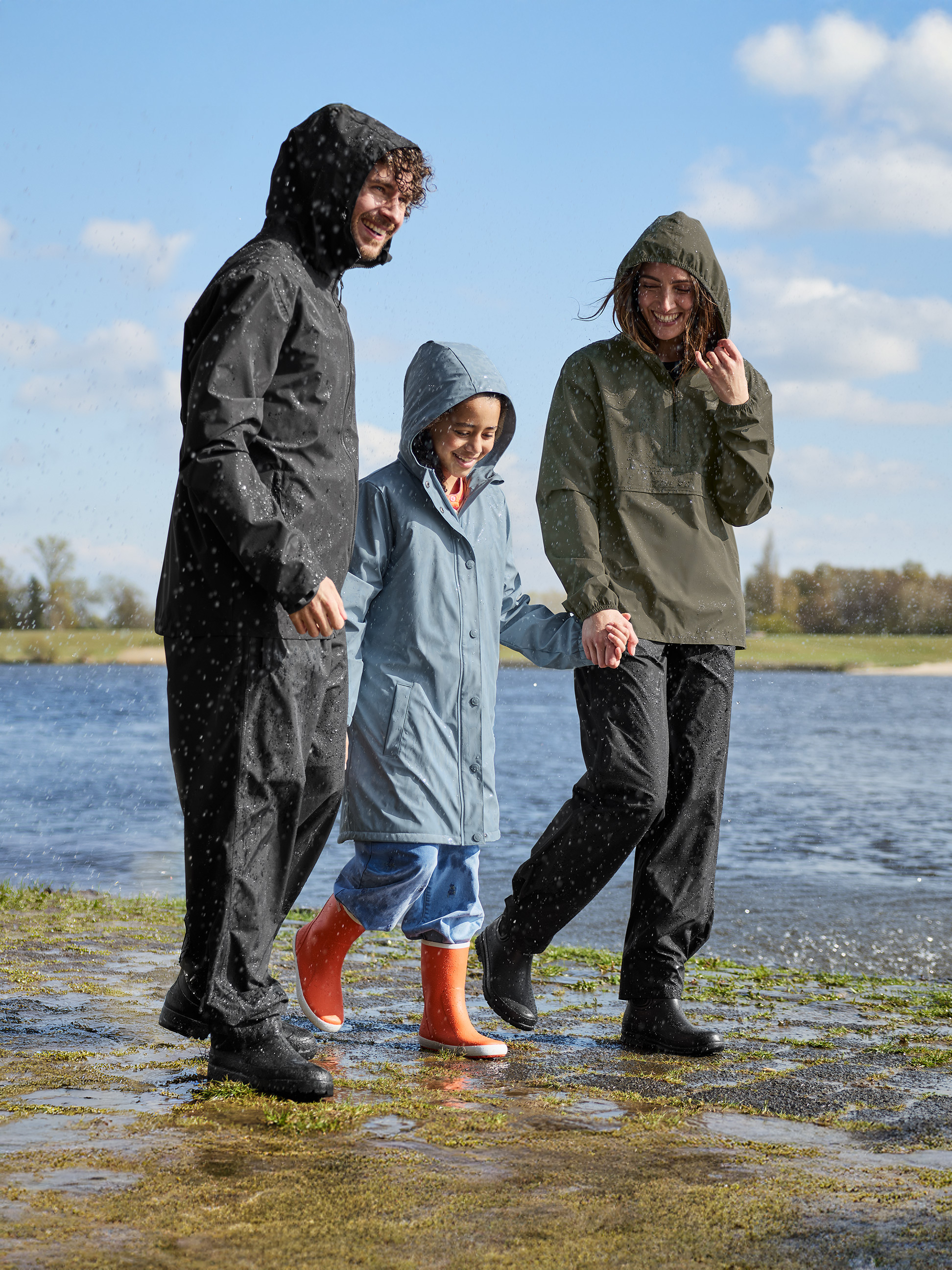 Lachende familie in regenjassen en laarzen, lopend langs het water.