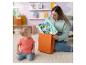 Een vrouw haalt karaktervormige babyspeeltjes uit een oranje cadeauzak, terwijl een baby toekijkt.