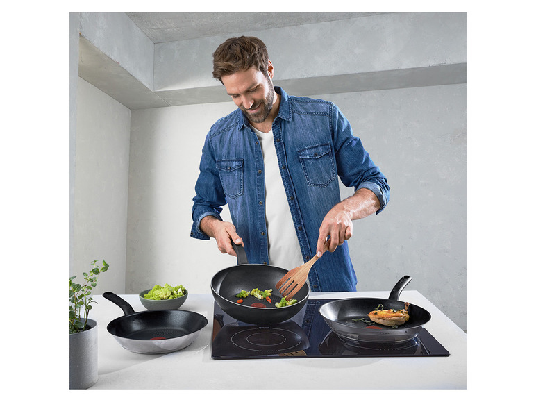 Een man kookt in de keuken met drie pannen op een inductiekookplaat.