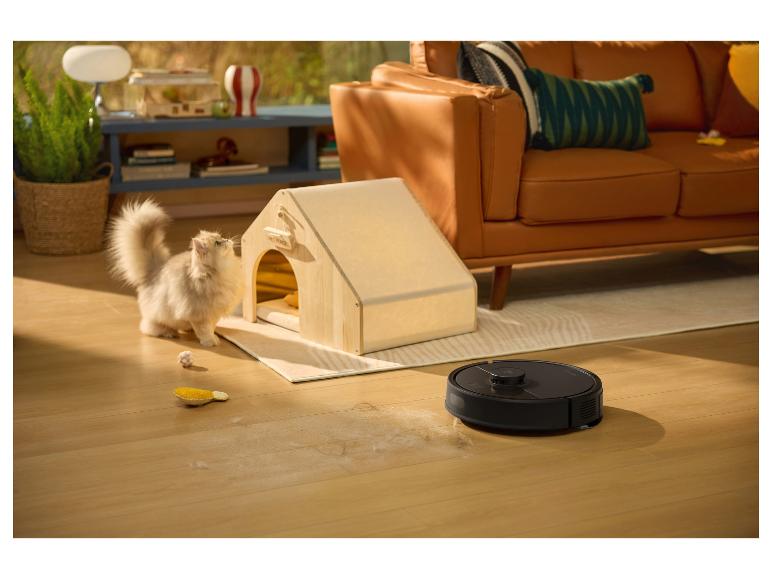 Robotstofzuiger reinigt kattenhaar op houten vloer, met een kat en een houten huisje.