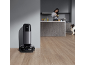 Robotstofzuiger in een moderne keuken met een vrouw die eten bereidt en een hond.