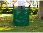 Persoon in de tuin met een groene tuinafvalzak vol bladeren.