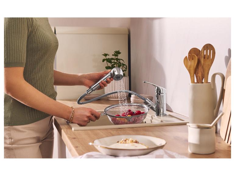 Vrouw wast bessen in een vergiet met uittrekbare kraan in een moderne keuken.