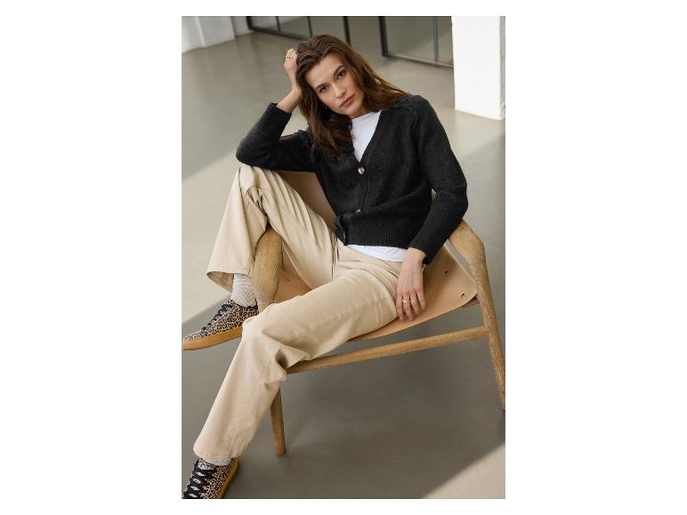 Vrouw in zwart vest, beige broek en sneakers met luipaardprint zit op een stoel.