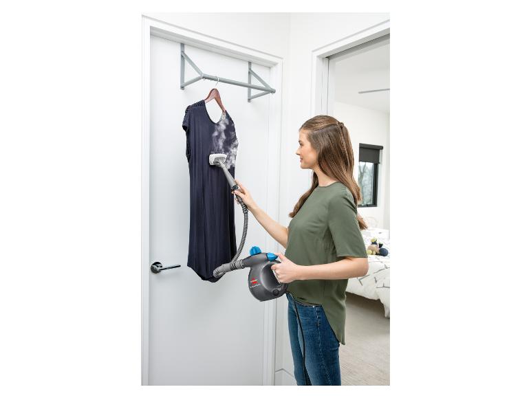 Vrouw gebruikt een Bissell Steam Shot handstomer om een marineblauwe jurk glad te maken.