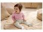Baby in roze overslagbody en geribde legging zit op een kleed.