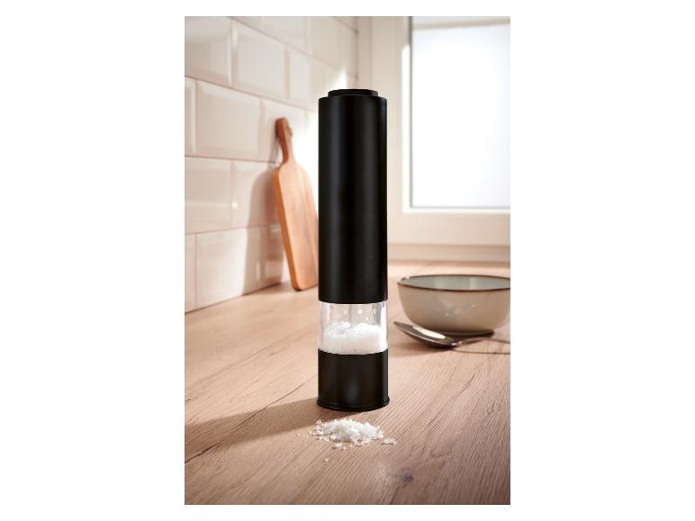 Zwarte elektrische zoutmolen met grof zout op een houten aanrecht.