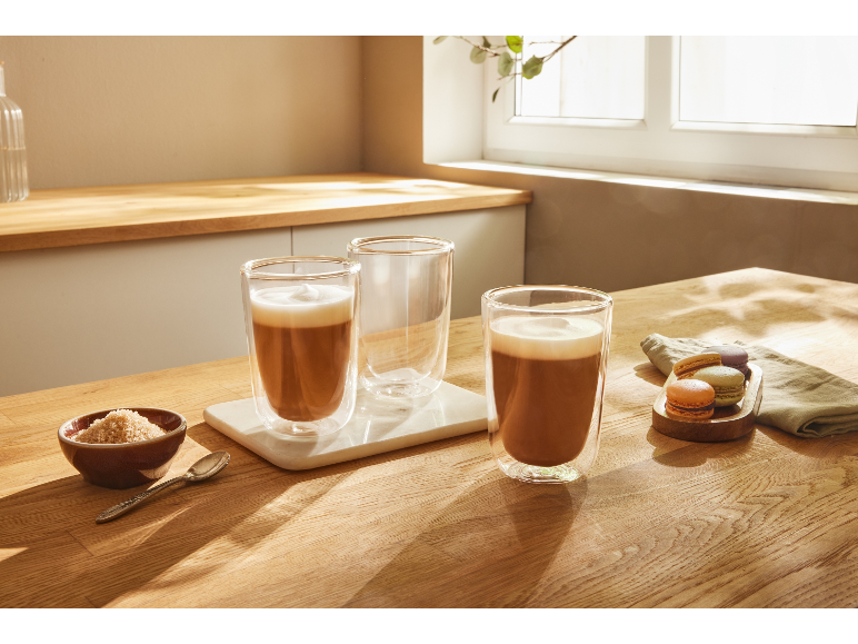 Twee glazen latte en gebak op een houten tafel.