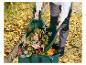 Persoon schept herfstbladeren in een groene tuinafvalzak met bladgrijpers.