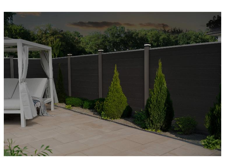 Buitenpatio met een ligbed en een donkere privacy schutting met geïntegreerde verlichting.