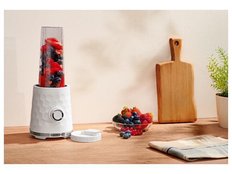 Witte persoonlijke blender met bessen, een fruitschaal en een houten snijplank op een aanrecht.