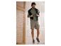 Man in een groen T-shirt, beige cargoshort en grijze sneakers, lachend binnenshuis.