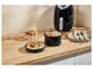 Airfryer met accessoires: spiesjes, bakvorm en pizzapan op een aanrecht.