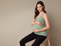 Een zwangere vrouw draagt een groene tanktop en zwarte broek.