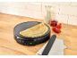 Crêpe maker met crêpes, melk, jam en aardbeien op een houten aanrecht.