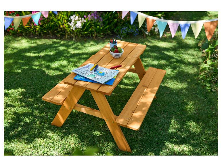 Houten picknicktafel voor kinderen met kleurboek, kleurpotloden en fruit in een tuin.