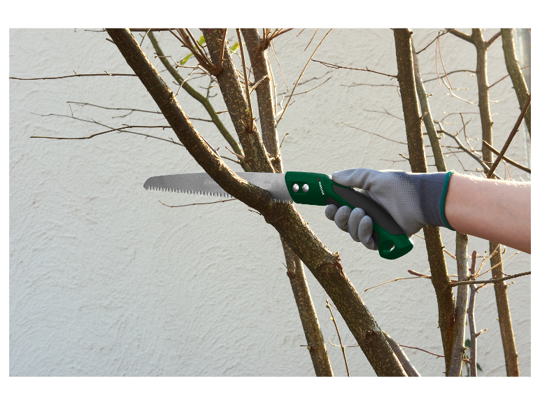 Een hand in handschoen gebruikt een Parkside handzaag om een boom te snoeien.