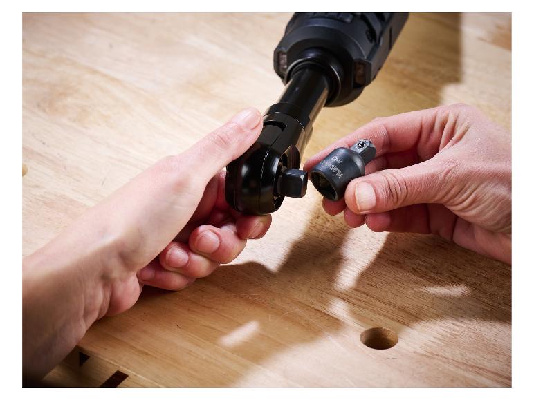 Handen bevestigen een dopsleuteladapter aan een ratelsleutel op een houten werkbank.