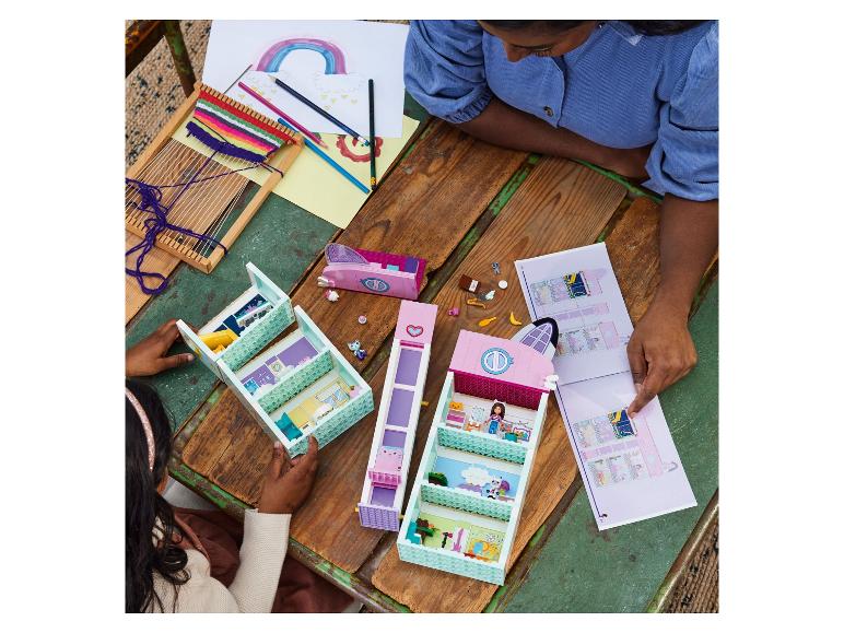 Twee meisjes bouwen een LEGO Friends set op een houten tafel met tekeningen en weefwerk.