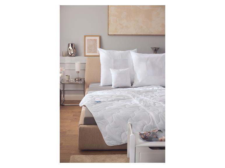 Wit dekbed en kussens op een beige bed in een slaapkamer met houten vloer.