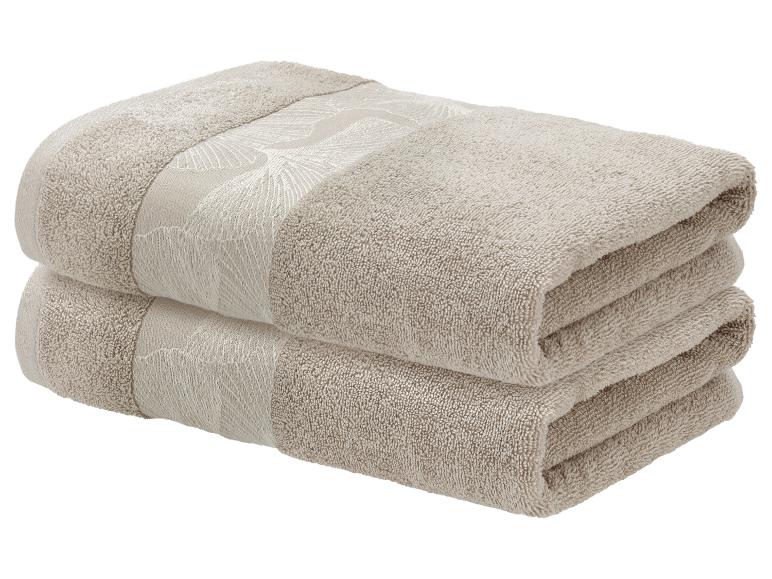 Twee gestapelde beige handdoeken met een decoratief bladpatroon.