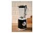 Zwarte retro blender met glazen kan op een houten aanrecht, tegen een betegelde muur.