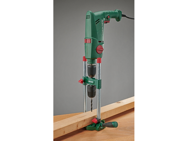 Groene elektrische boormachine met boorstandaard, boort in een houten plank.