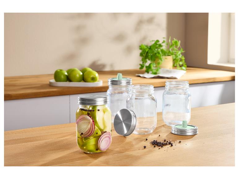Glazen potten met metalen deksels, één gevuld met ingemaakte appels en uien, op een houten aanrecht.