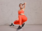 Vrouw in oranje leggings en sportbeha met dumbbells.