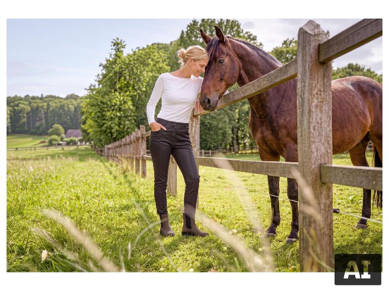 Vrouw in ESMARA® slim fit broek staat bij een hek met een paard. [AI-gegenereerde afbeelding]