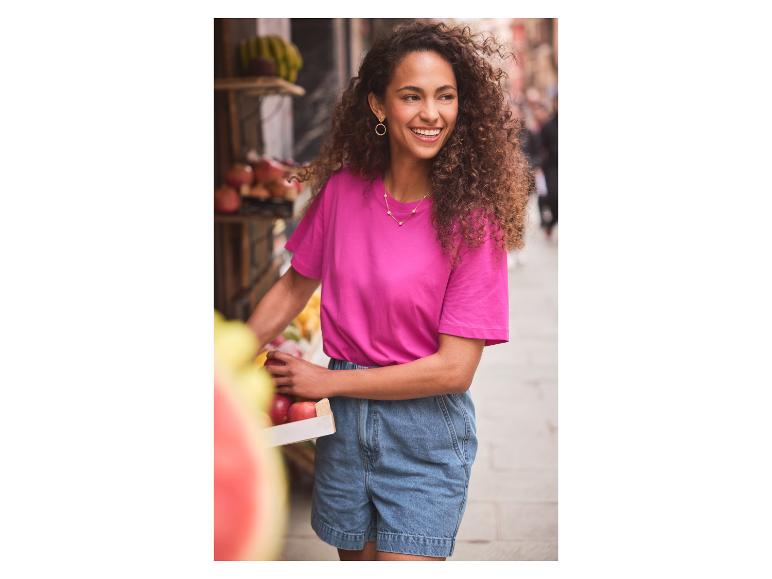 Lachende vrouw in roze t-shirt en jeans shorts fruit aan het kopen.