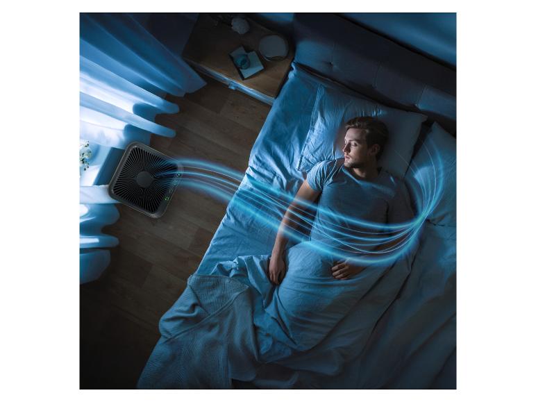 Luchtreiniger blaast koele lucht over slapende man in donkere kamer.